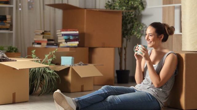 Relaxed woman holding a cup of tea sitting on the floor surrounded by moving boxes