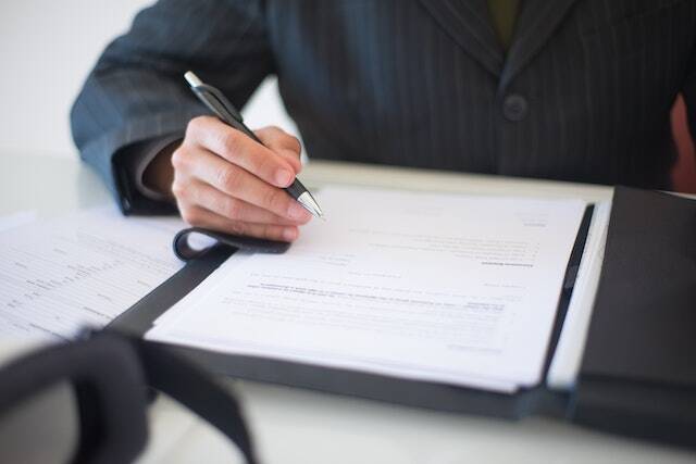 person-in-a-blue-suit-holding-a-pen-to-sign-a-contract-in-front-of-them